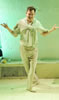 Aguecheck in white polo shirt and cream-colored pants, with white sweater tied around his shoulder, stands with legs crossed and hands out in triumph, Toby in white cocktail dress and pearl necklaces reading a letter and Maria in white dress, glasses, and her hair up in a bun, looking over her shoulder